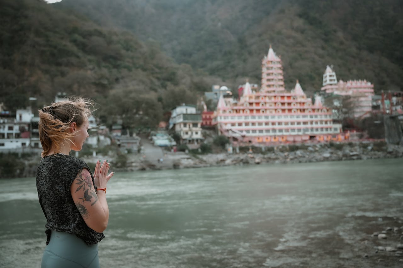 gallery-4 A woman practices yoga by the Ganges River in Rishikesh with a temple in the background.