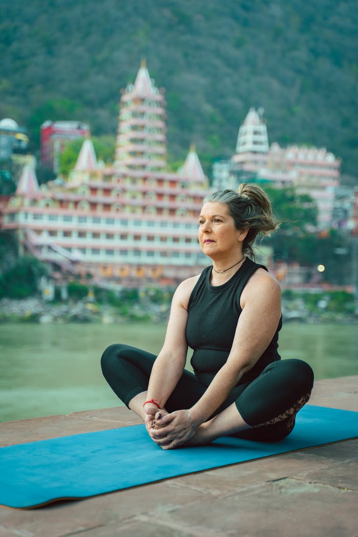 gallery-5 Adult woman doing yoga on a mat by the river with iconic Rishikesh skyline in the background.