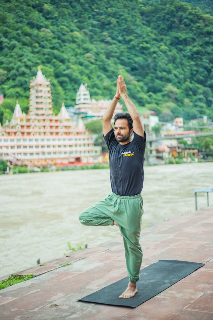 gallery-6 A man performing yoga on a riverside terrace in Rishikesh with temples in the background.