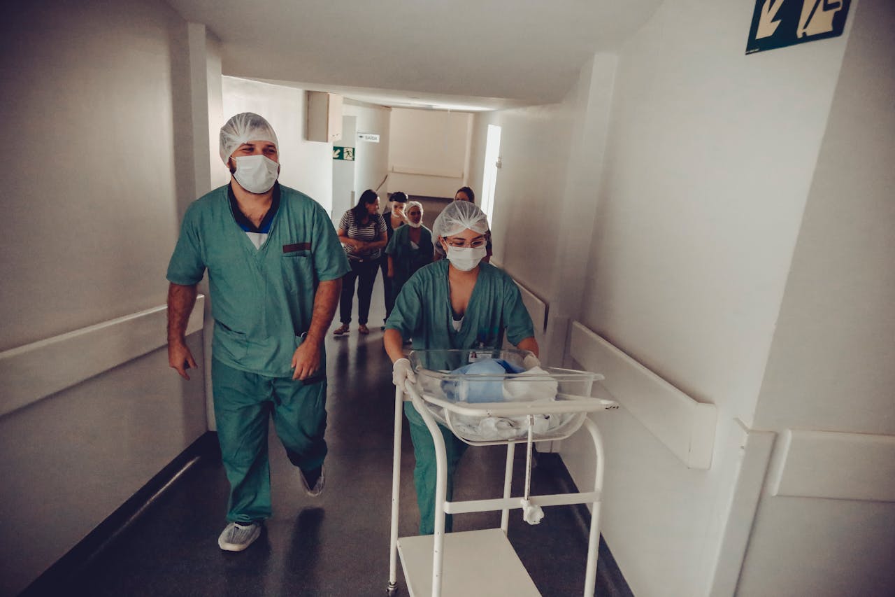 about-01 Healthcare workers in surgical attire transporting a newborn in a hospital corridor.