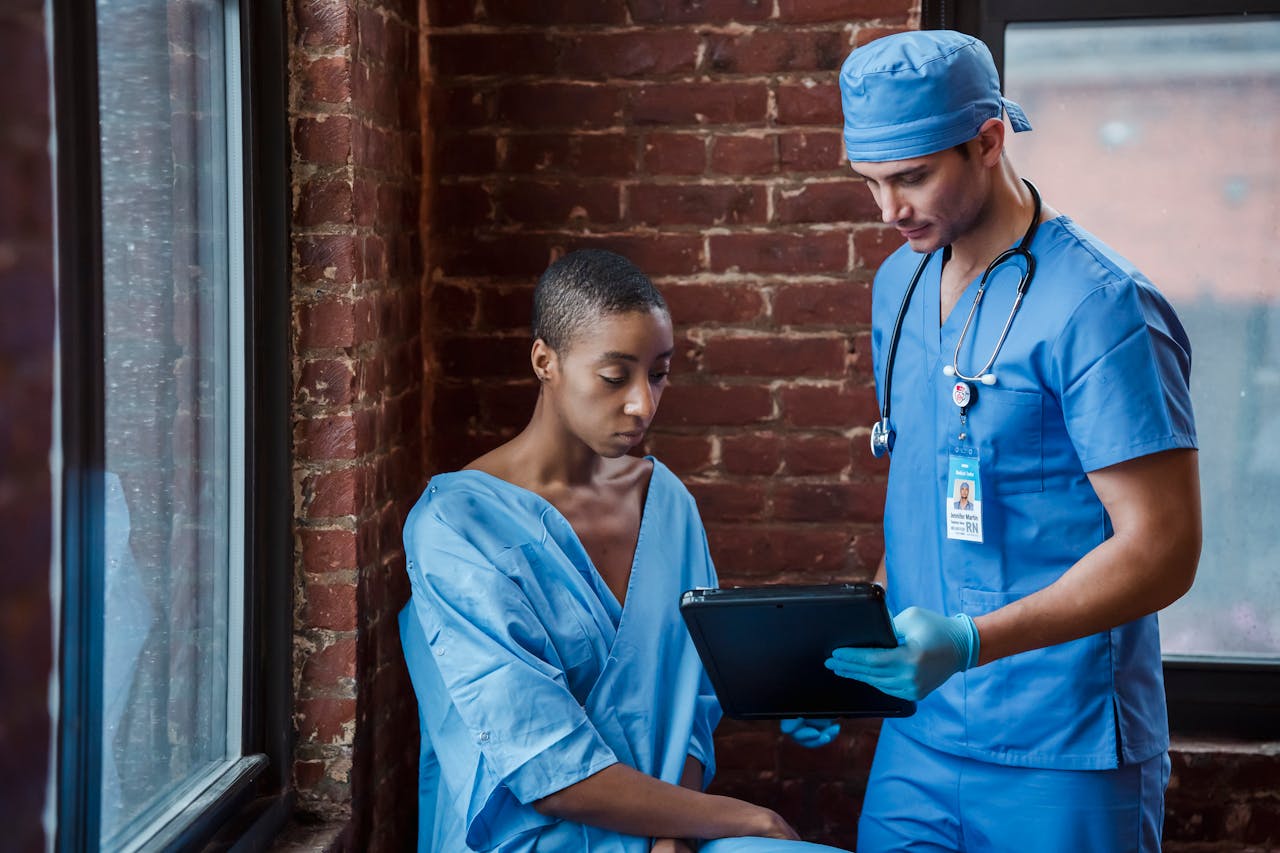 services-03 Thoughtful doctor in uniform and gloves showing diagnosis to African American female patient with short hair in blue medical robe in hallway of hospital in daytime
